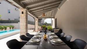 A covered outdoor dining area with a pool, stone columns, and black chairs. - Villa Molindrio by Villas Guide (Porec)