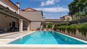 Una piscina con zona de patio, pilares de piedra y vistas de edificios circundantes.