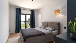 Un dormitorio moderno con cama, mesita de noche, planta en maceta y vistas al exterior.