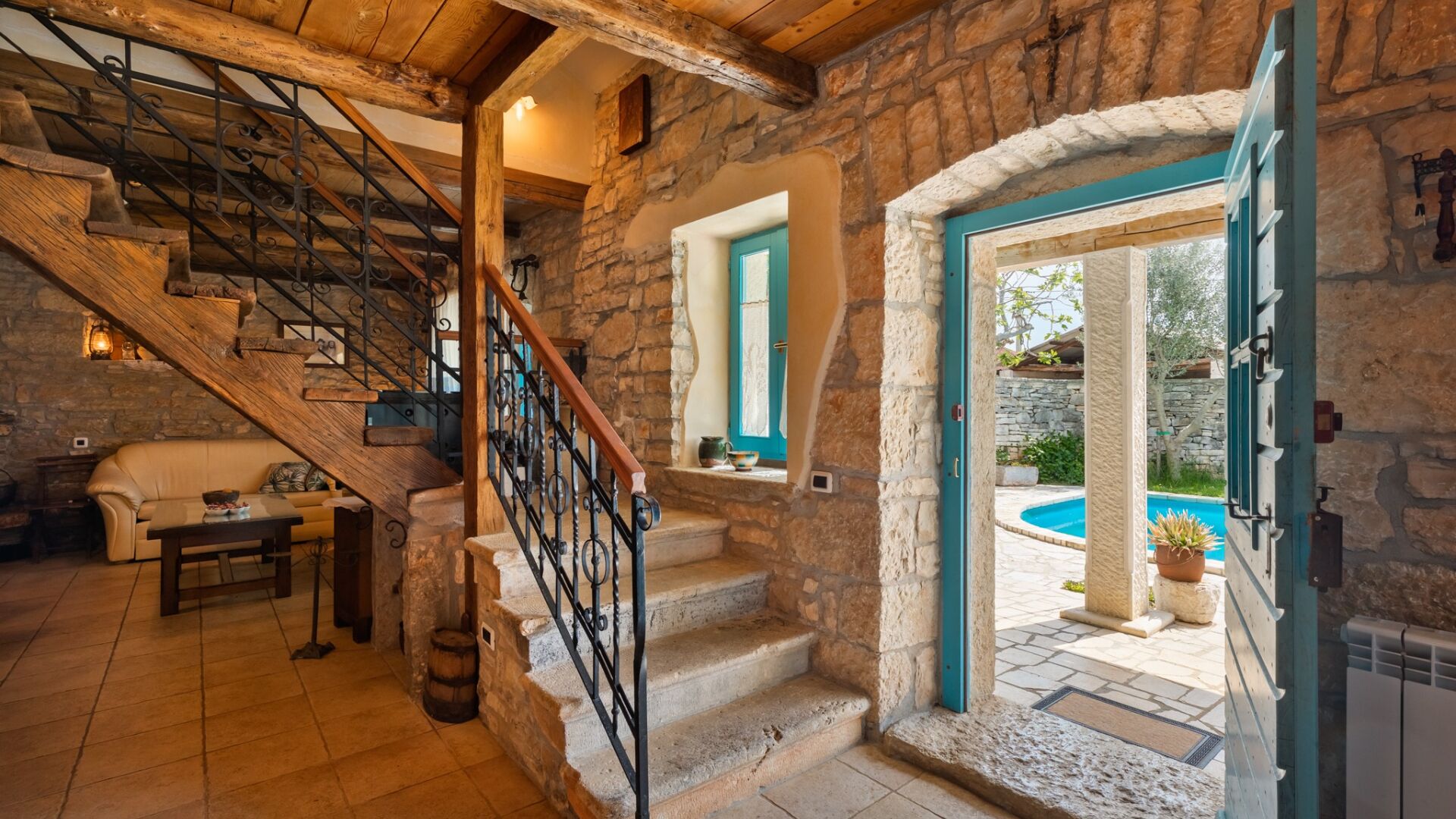 A rustic interior with stone walls, a wooden staircase, a pool, and a cozy seating area.