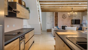 A modern kitchen with wooden cabinets and a built-in oven, a dining area with a wooden table, and a living room with a sofa and a TV. - Villa Monte by Villas Guide (Vižinada)