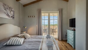 A bedroom with a large bed, a TV, a dresser, and a balcony with outdoor furniture. - Villa Monte by Villas Guide (Vižinada)