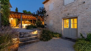 A stone building with a covered patio, steps leading to a door, and outdoor lighting.
