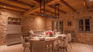 A stone-walled dining area with a wooden ceiling, a bench, and a table set for four.