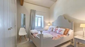 A bedroom with a large bed, a chair, a bedside table, and a window with curtains.