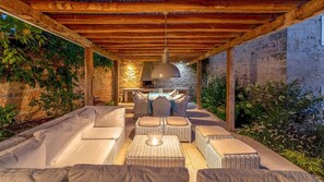 An outdoor seating area with a stone wall, a stone fireplace, and a hanging light fixture.