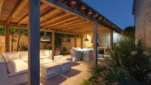 Um pátio externo com móveis de vime, paredes de pedra e uma estrutura de pérgola.