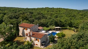 Una casa de piedra con piscina, rodeada de un bosque frondoso.