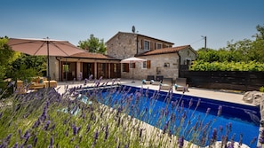 Uma casa de pedra com piscina, área de estar externa e plantas de lavanda.