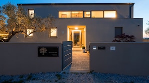 A modern villa with a gated entrance, a tree sign, and a number sign.