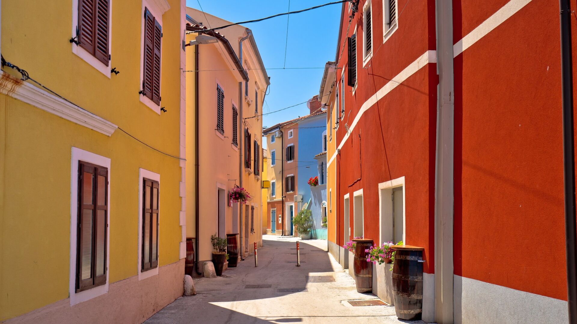 A narrow street with colorful buildings, a clear sky, and potted plants along the sidewalk.
