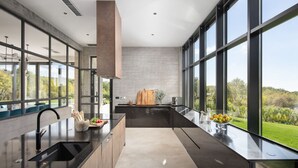 A modern kitchen with large windows, a central island, and a view of the outdoors.