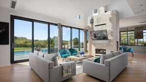 A modern living room with a fireplace, large windows, and a pool view.