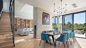 A modern interior with a dining area, a staircase, and a large window offering a view of the outdoors.