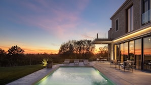 A modern house with a swimming pool, outdoor seating, and a glass-enclosed patio.