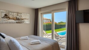 A bedroom with a bed, a painting, a TV, and a view of a swimming pool. - Villa Blagdan by Villas Guide (Porec)
