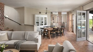 A spacious living area with a sofa, a dining table with chairs, a kitchen with a brick wall, and a sliding glass door leading to an outdoor area.