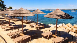 A beachside lounge area with thatched umbrellas and lounge chairs facing the sea.