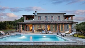 A two-story stone house with a swimming pool, outdoor seating, and a covered patio area.