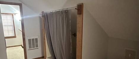A small, narrow room with a shower, toilet, and a window.