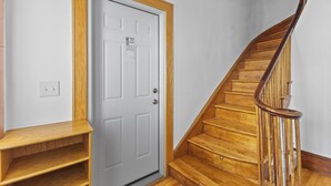Una escalera de madera con barandilla, una puerta blanca con marco de madera y un interruptor de luz en la pared.