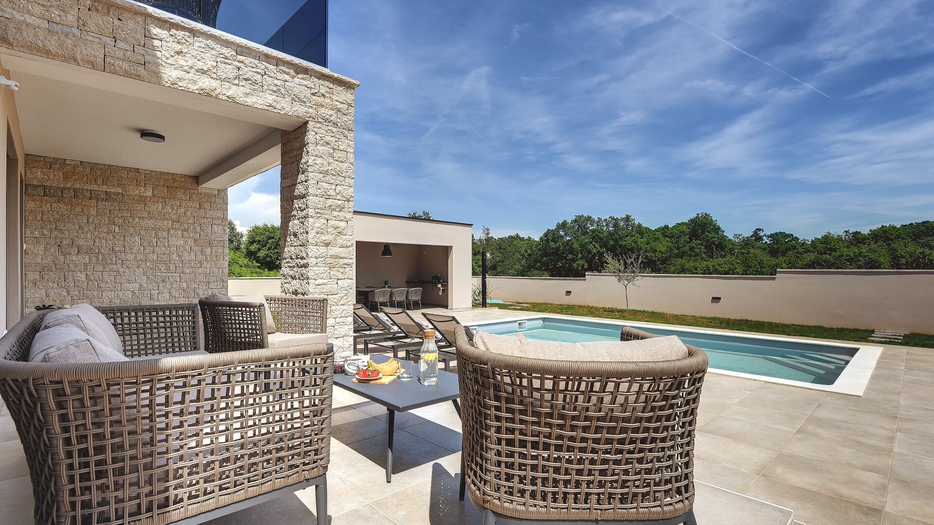 An outdoor patio with wicker furniture, a pool, and a stone wall.