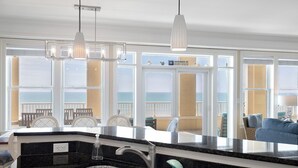 Una cocina con un ventanal grande, un lavamanos y una zona de comedor con sillas.
