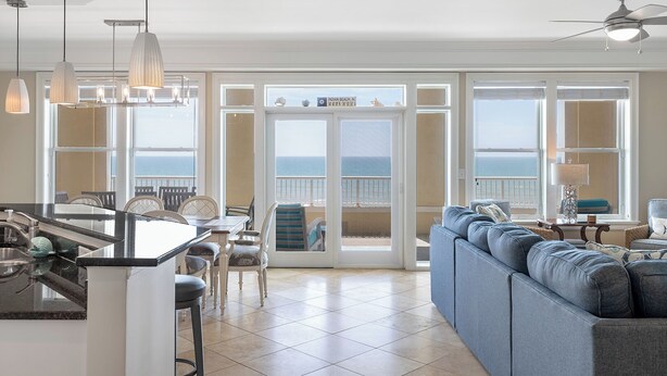 Amplia sala de estar con un gran ventanal con vistas al océano, un área de cocina y un ventilador de techo.