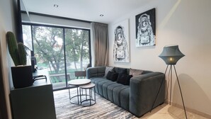 Un salon moderne avec un canapé gris, une petite table ronde, un lampadaire et un cactus posé sur une étagère.