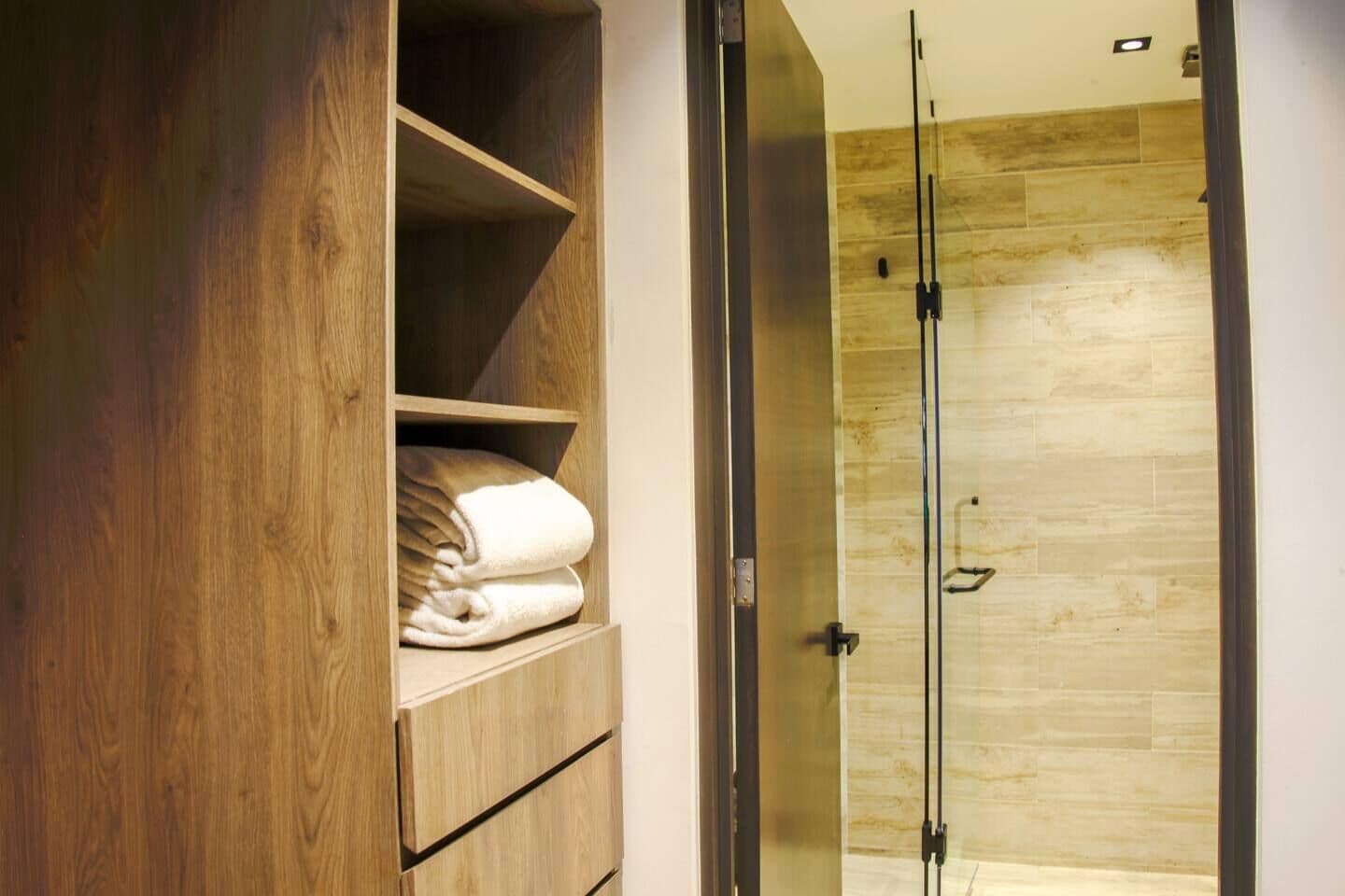 Ein hölzerner Kleiderschrank mit gefalteten Handtüchern und einer Duschkabine aus Glas in einem Badezimmer.