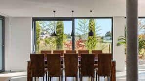 A dining area with a table and chairs, large windows, and a view of trees and buildings. - Villa Aria by Villas Guide (Višnjan)