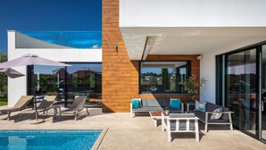 A modern outdoor pool area with lounge chairs, umbrellas, and a seating area with cushions. - Villa Aria by Villas Guide (Višnjan)