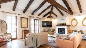A cozy living room with exposed wooden beams, a fireplace, a television, and comfortable seating.