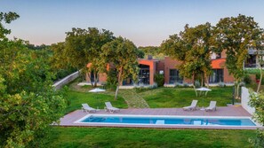 Un área de piscina moderna con una piscina rectangular, rodeada por una terraza de madera, y adyacente a un edificio con fachada de vidrio.