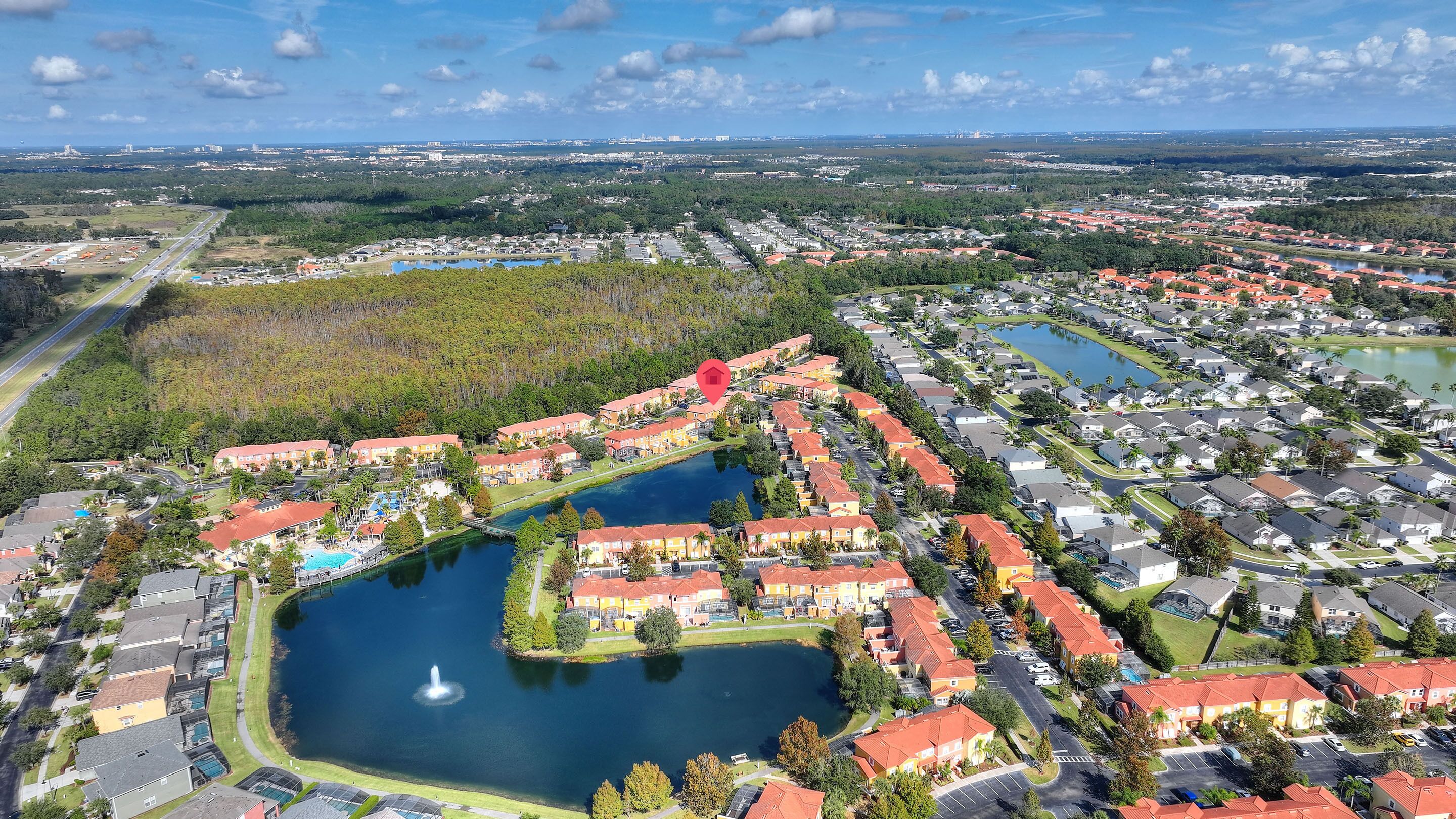 An aerial view of a residential area with a central lake, surrounded by houses with red roofs, and a road running parallel to the lake.