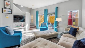 A living room with a blue armchair, beige sofa, and a television. - Serene Stay 3bed at Terra Verde (Kissimmee)