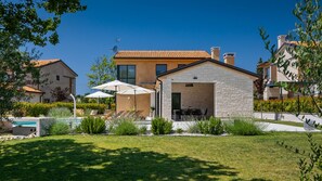 Une maison moderne avec une façade en pierre, une piscine et un espace salon extérieur.