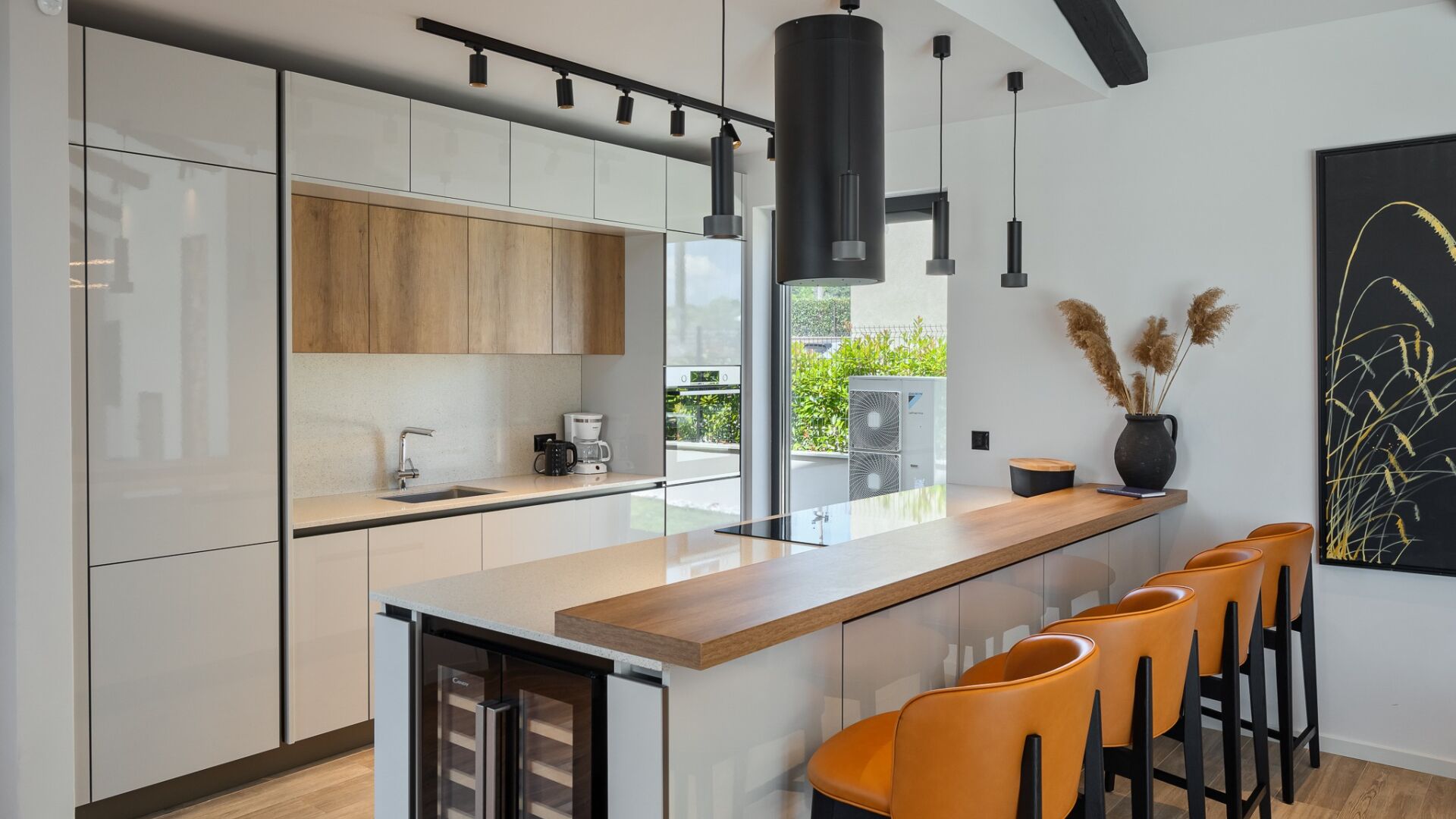 Een moderne keuken met een centraal eiland, barkrukken en een groot raam.