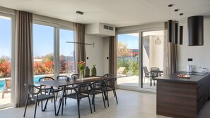 Ein moderner Essbereich mit Blick auf den Pool, großen Fenstern und einer Küche mit integrierter Kochinsel.