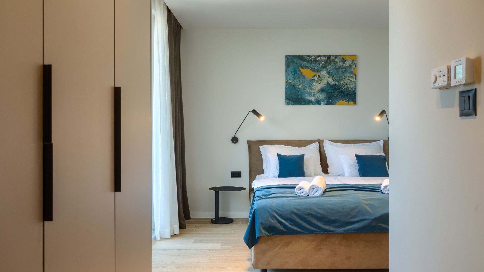 Une chambre d’hôtel avec un lit, un tableau au mur, une lampe et un thermostat.