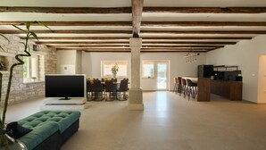 A spacious living area with exposed wooden beams, a flat-screen TV, a green sofa, a dining table with chairs, and a kitchen area with a bar. - Villa Kave by Villas Guide (Grožnjan)