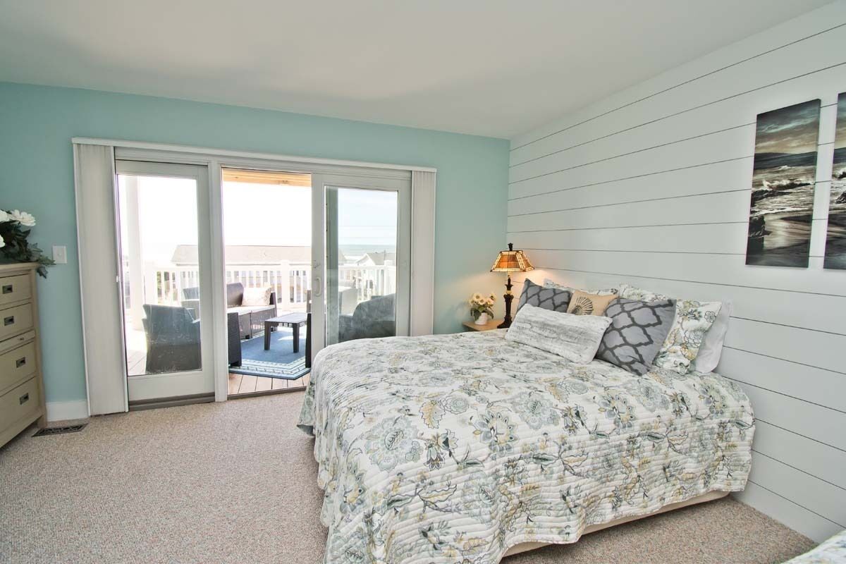 A bedroom with a bed, a nightstand, a lamp, and a view of the outside.
