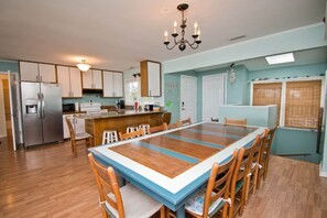 A spacious kitchen with a large dining table, wooden chairs, and a built-in island. - Decks Ahoy, Oceanfront House in Emerald Isle, NC! (Emerald Isle)