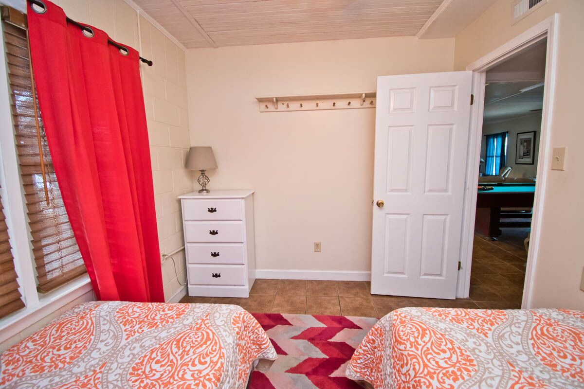 A bedroom with two beds, a dresser, a lamp, and a door leading to another room.