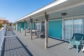 A covered outdoor area with a table and chairs, a green chair, and a railing. - Decks Ahoy, Oceanfront House in Emerald Isle, NC! (Emerald Isle)