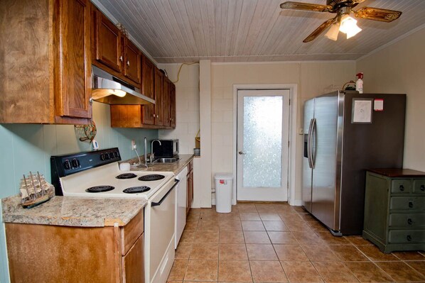 A kitchen with wooden cabinets, a stove, a refrigerator, and a ceiling fan.