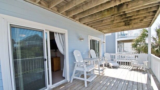 A covered deck with white chairs and a table, a sliding glass door, and a wooden ceiling. - Dock Holiday, Oceanview House in Atlantic Beach, NC! (Atlantic Beach)