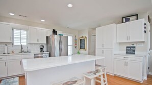 A modern kitchen with white cabinetry, a central island, and bar stools. - Dock Holiday, Oceanview House in Atlantic Beach, NC! (Atlantic Beach)