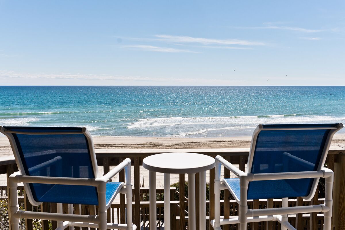 A deck with two chairs and a table overlooking a beach with waves.