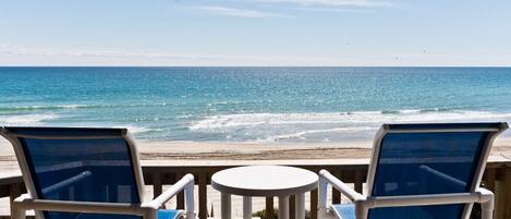A deck with two chairs and a table overlooking a beach with waves.